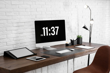 Modern workplace interior with computer and devices on table near brick wall
