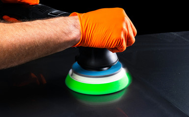 Car polish wax worker hands applying protective tape before polishing. Buffing and polishing car. Car detailing. Man holds a polisher in the hand and polishes the car. Tools for polishing
