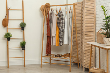 Stylish wooden table and rack with clothes in modern room interior