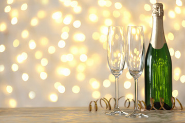 Empty glasses and bottle of champagne on table against blurred lights. Space for text