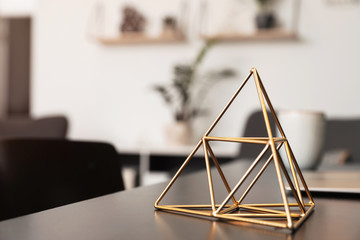 Decorative metal pyramid on table in room. Modern interior element