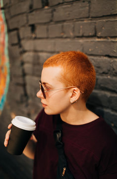 young androgyne woman with short red hair drinking coffee on str