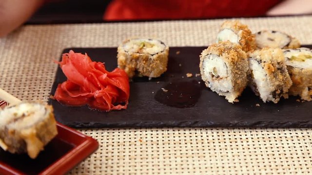 Girl eating sushi rolls with chopsticks in a Japanese restaurant. Hand with chopsticks while taking sushi. Serving rolls on a black slate tray