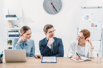 pensive recruiter in glasses looking at coworker holding pen near notebook