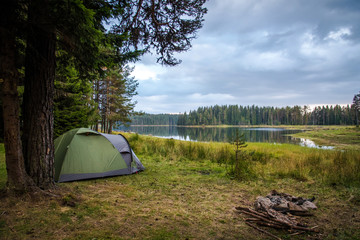Camping near a lake in a cloudy day - tent and a fireplace near a lake. 