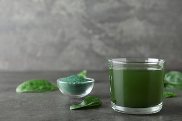 Glass of spirulina drink, spinach and powder on table against grey background. Space for text