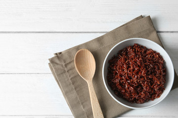 Bowl of boiled brown rice and spoon on table, top view. Space for text