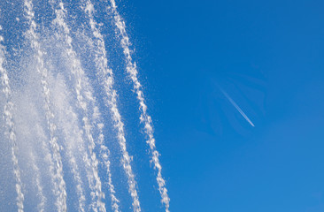 Jets and splashes of water fountain against the blue skyCondensation track of a jet plane against the sky and a fountain.