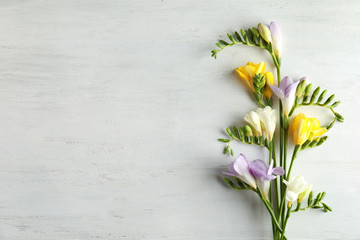 Beautiful fresh freesia flowers on wooden background, flat lay. Space for text