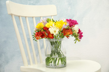 Beautiful bright freesia flowers in vase on chair