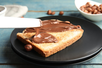 Fototapeta na wymiar Spreading sweet chocolate cream onto toast on table, closeup