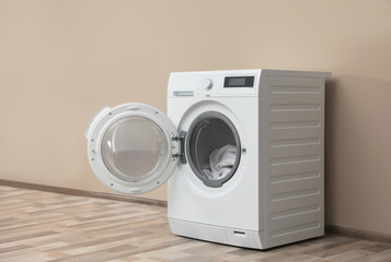 Modern washing machine with laundry near color wall, space for text