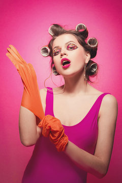Cheeky girl with latex gloves posing on pink background in body, with curlers on head. Pretty sexy woman with sweet makeup attractively posing in studio.