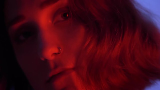 Closeup shoot of young attractive caucasian female with naked shoulder seductively looking at camera with neon blue and red background