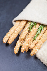 Italian grissini bread sticks with sesame and rosemary herb on black board background.