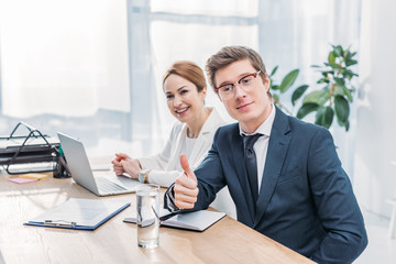 handsome recruiter in glasses showing thumb up near cheerful coworker