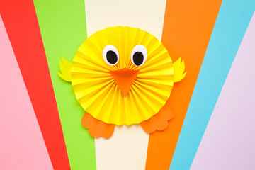 Happy yellow chick folded and created from paper on colorful background. 