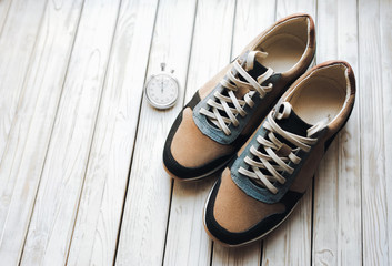 Two beige sport shoes (sneakers) from suede with stopwatch on white rustic wooden background....
