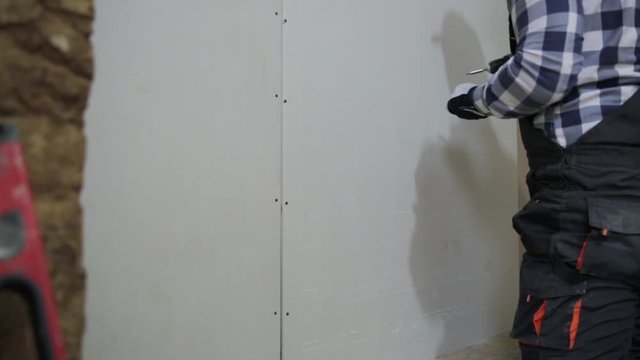 Man installing plasterboard sheet to wall for attic room construction