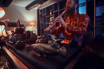 Tradition, health, harmony. Chinese tea ceremony. Tea master in kimono performs in the dark room with a wooden interior, playing on a bamboo flute