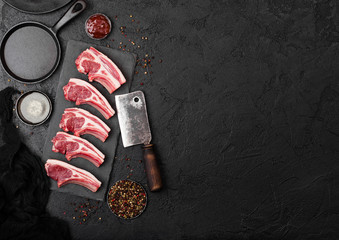Fresh raw butchers lamb beef cutlets on stone board with vintage hatchet on black stone background. Salt and pepper with pan kitchen towel