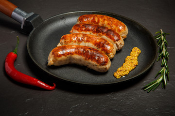 four fried sausages on round black pan with granular mustard
