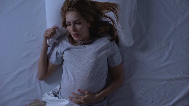 Exhausted pregnant female suffering nausea, wiping mouth with tissue, weakness