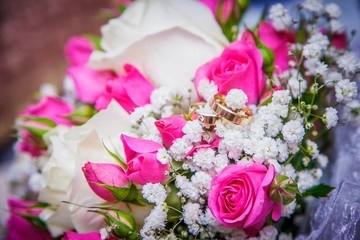 Wedding rings on the bride's bouquet from the pink and white roses. Close-up. On the photo, there are no people only golden rings and flowers. Background is blurred.