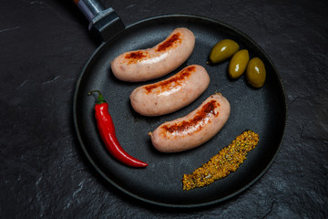 top view of on round black pan with three fried sausages