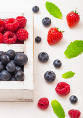 Fresh raw organic berries in white wooden box on white kitchen table background. Close up. Strawberry, Raspberry, Blueberry and Mint leaf