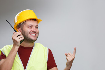 Image of cheerful builder in yellow helmet talking on walkie-talkie pointing his finger up in studio.
