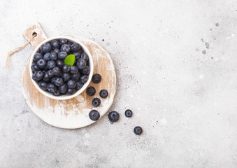Fototapeta na wymiar Fresh raw organic blueberries with leaf in white china bowl on stone kitchen background. Top view. Space for text