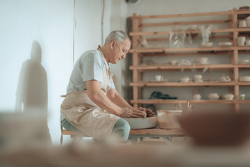 Side view of craftsman working on potter's wheel in his workshop