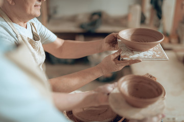 High angle of male craftsman looking at his ceramic bowl in workshop