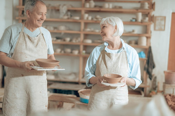 Elderly happy clay masters looking at each other in workshop