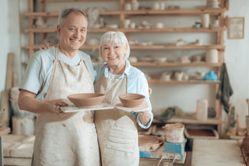 Elderly happy clay masters looking at camera and showing their work