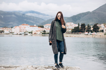 Beautiful young trendy girl walks near the sea against the backdrop of Tivat in Montenegro.