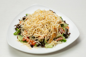 salad of fresh vegetables and greens, with chicken meat and cheese, on a white plate