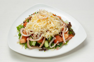 salad of fresh vegetables and greens, with squid rings and cheese, on a white plate