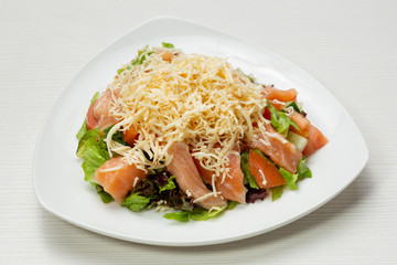 salad with fresh cucumbers, tomatoes and greens, with salmon and cheese, on a white plate
