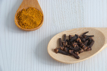 Top view of two wooden spoons with spices. Cloves and curry on white wooden background