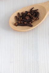 Top view of a wooden spoon with cloves on white wooden background with copy space