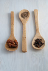Top view of three wooden spoons with spices. Cayenne, cumin and cloves on white wooden background