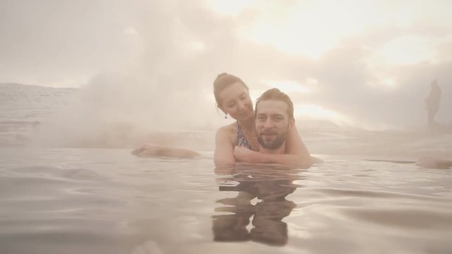 Young pretty couple enjoying the hot pool while relaxing in open pool at Winter sunny day
