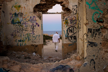 Man walking at the beach, with an urban graffiti building with a sunset view in Spain Torrevieja. Walking person and an old ruined building.