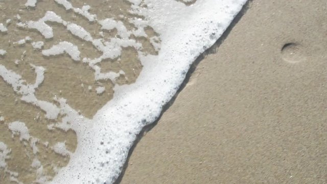 Footprints in the sand. The wave washes away the footprint of a person.