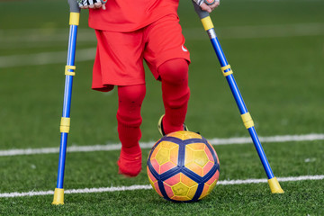 Legs of disabled football plaer with ball and crutches.