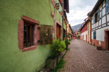 Street with old houses in a small town. France. Alsace. In the foreground is the green wall of the house. And the window with shutters. There is a road paved with stone. Background.