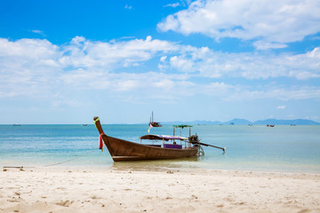 Fototapeta na wymiar Asian taxi. Long-tailed boat on a tropical white sand beach. Blue sky and sea, mountains on the horizon. It is cloudy.