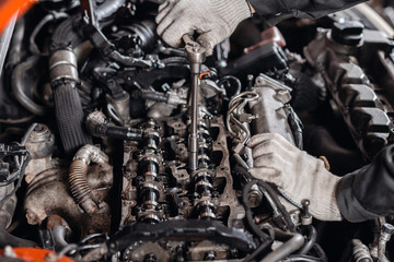 Unscrews the nut with the tool. Repairing of modern diesel engine, workers hands and tool.